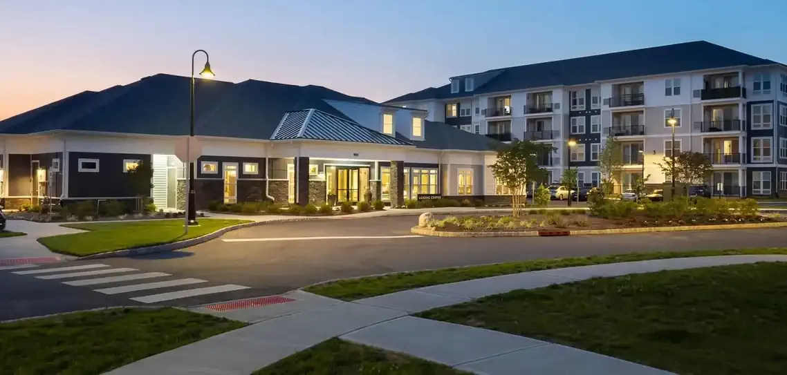 Wexford modern apartment building clubhouse with well-lit entrance and landscaped driveway at dusk.